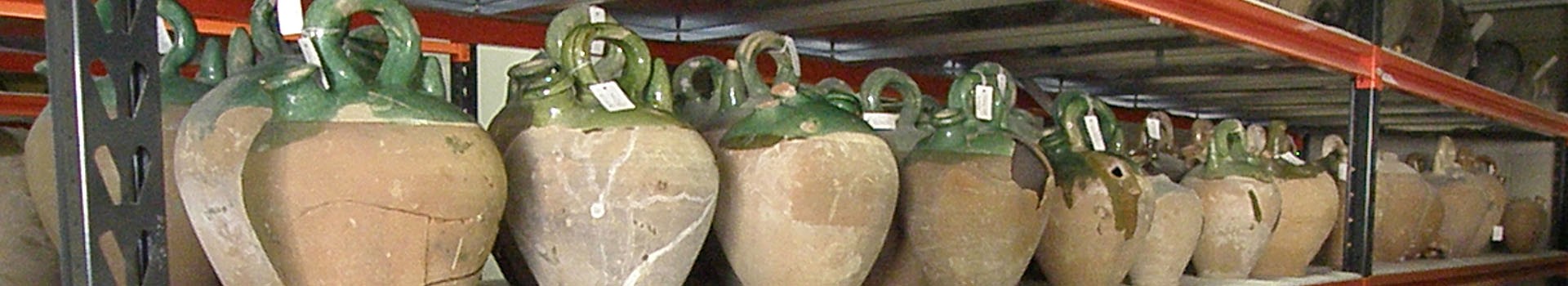 Medieval green and cream coloured pottery stands on racking shelves.