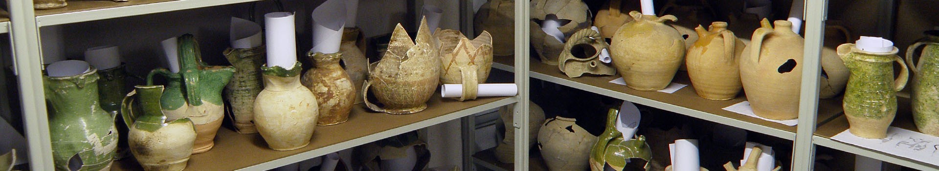 Cream and green coloured pottery stands on racking shelves.