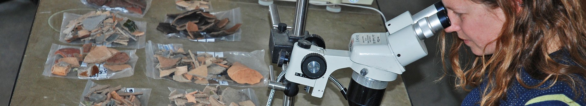 An archaeologist examines pottery through a microscope.