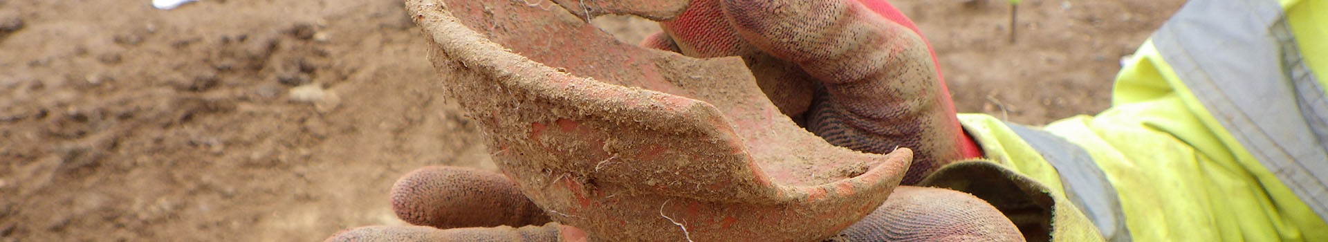 An archaeologist holds a newly excavated piece of ceramic in their hands.