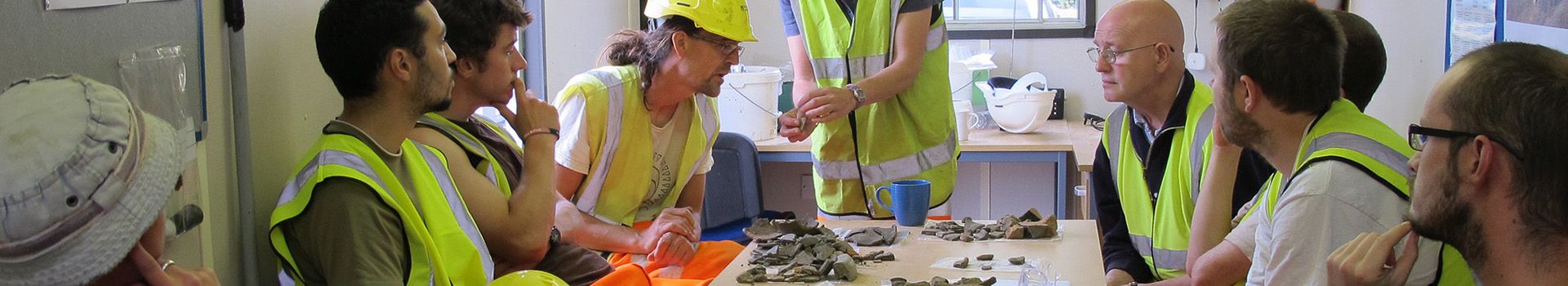 Archaeologists listen to a finds expert who displays recovered finds.