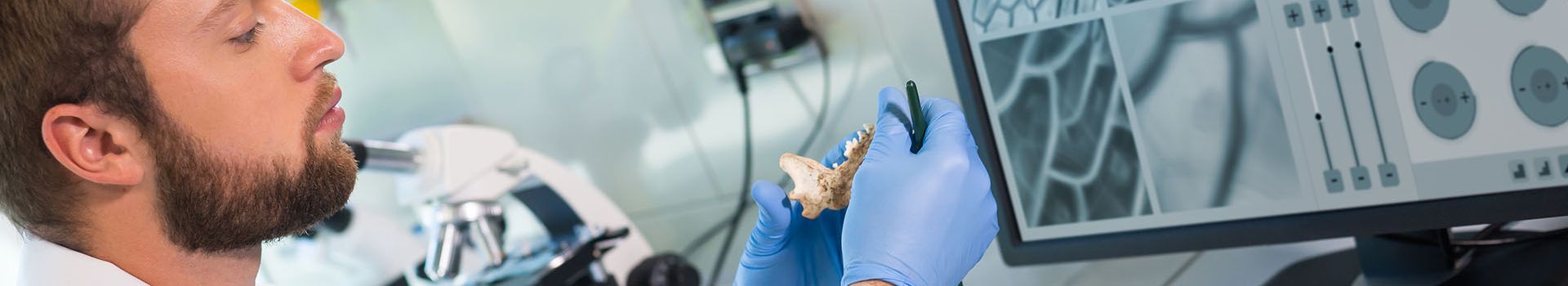 A laboratory technician in a white lab coat examines a small piece of bone.