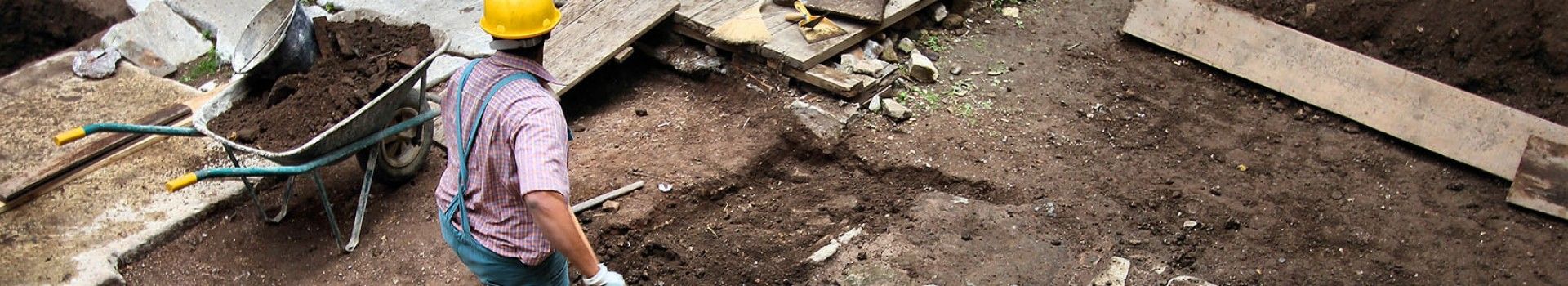 An archaeologist shovels earth into a barrow in a trench