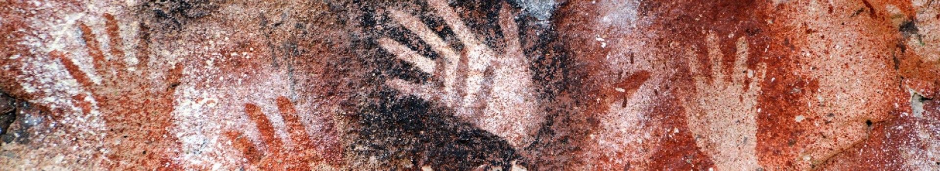 Ancient cave art depicting hand prints outlined with orange and black dyes.