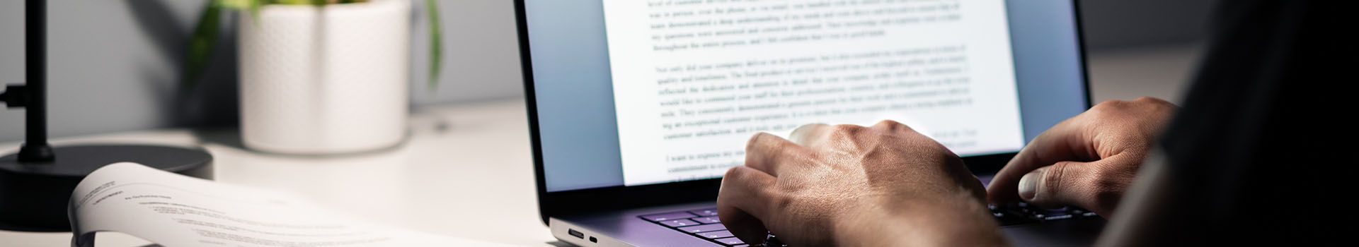 A person sits at a desk and types on a laptop next to a desk lamp.