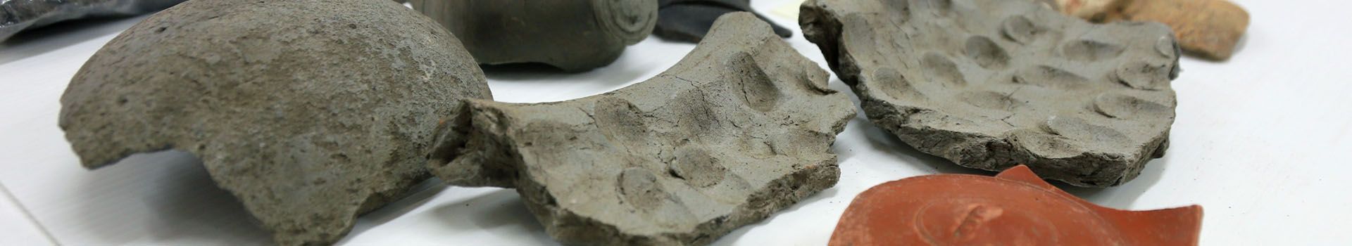 Fragments of grey and orange pottery lie on a white table.