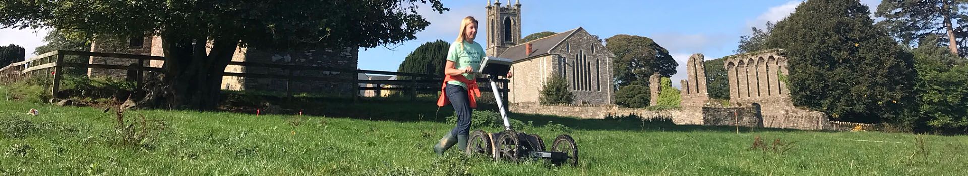 An archaeologist undertakes geophysical survey in a field with a church in the background.