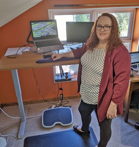 Sarajayne Clements stands in front of a desk with computer.