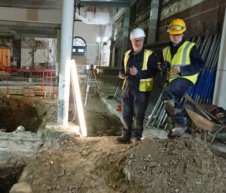 Stuart R Taylor stands beside an excavated trench inside a building.