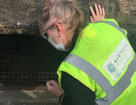 A woman in hi-vis clothing examines a metal grate.