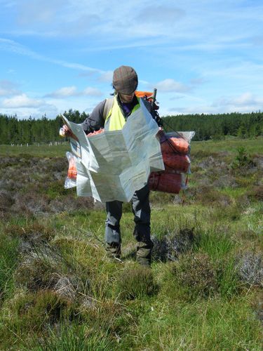 An archaeologist stands in a moorland landscape and examines a map.