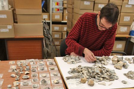 An archaeologist undertakes analysis of flint finds at a table.