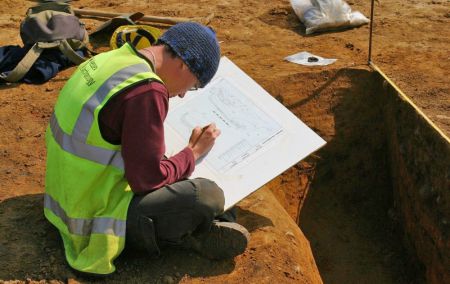 An archaeologist records an excavated trench using a pencil and paper.