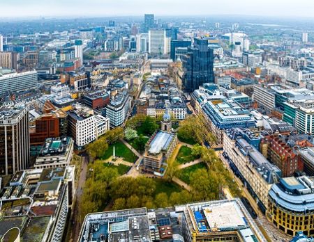 An aerial view over a cityscape with church surrounded by a green area positioned centrally.