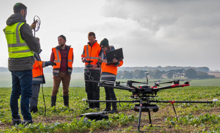 Archaeologists stand next to a drone and plan a flight in a green landscape.