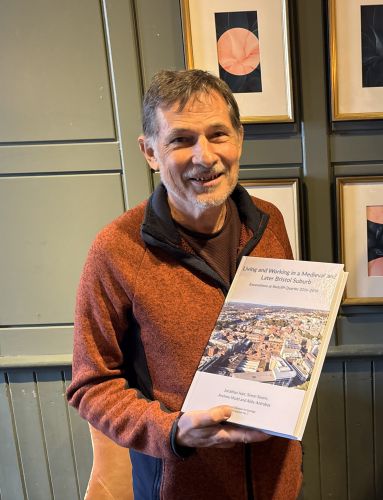 Andy Mudd smiling and holding his book