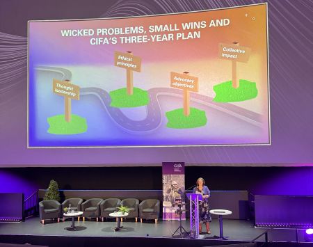 CIfA CEO Kate Geary on stage at CIfA Conference 2025 in front of a presentation that reads 'wicked problems small wins and CIfA's three year plan'
