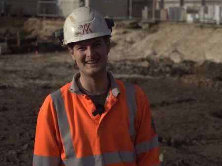 Photograph of Alex on site, wearing orange high vis and a white hard hat