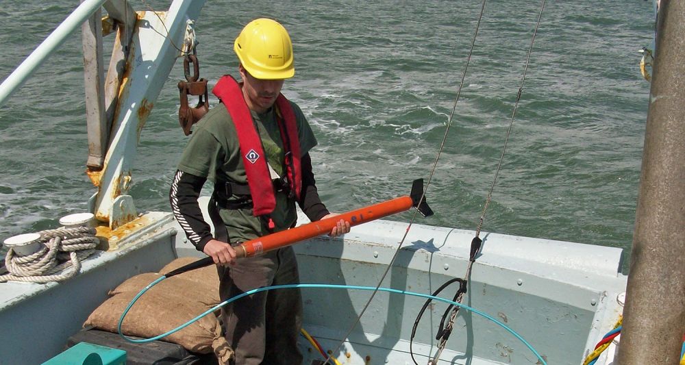 A marine archaeologist holds sonar equipment next to the edge of a boat on the sea.