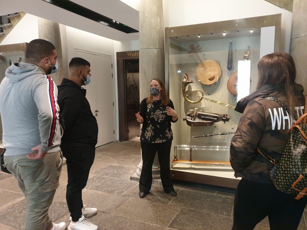 A person talks to a small group of people next to museum cases containing artefacts.