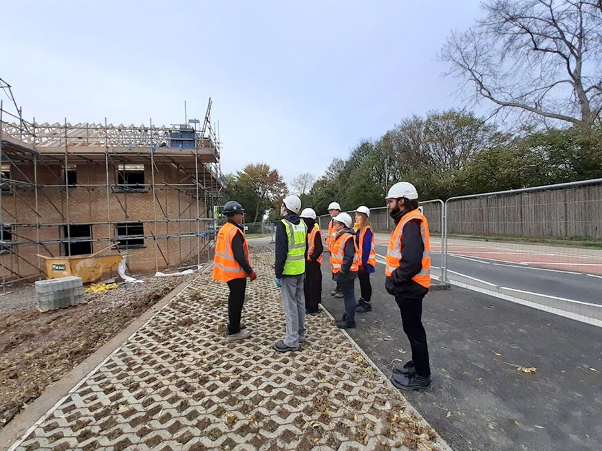 Archaeologists in hard hats and hi-vis clothing are tutored on a construction site.