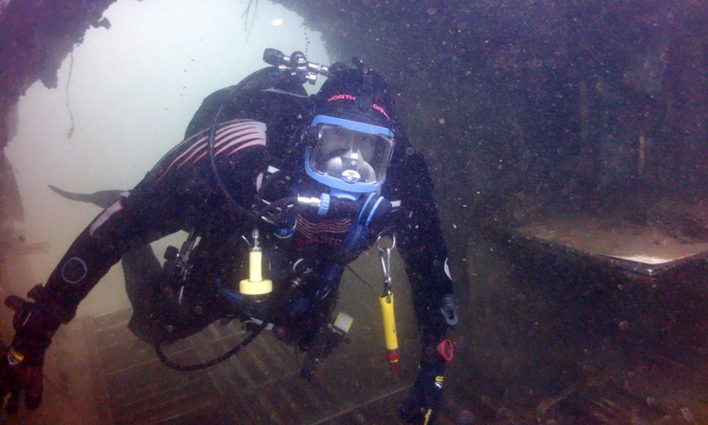 A diver looks at the camera whilst exploring a submerged wreck.