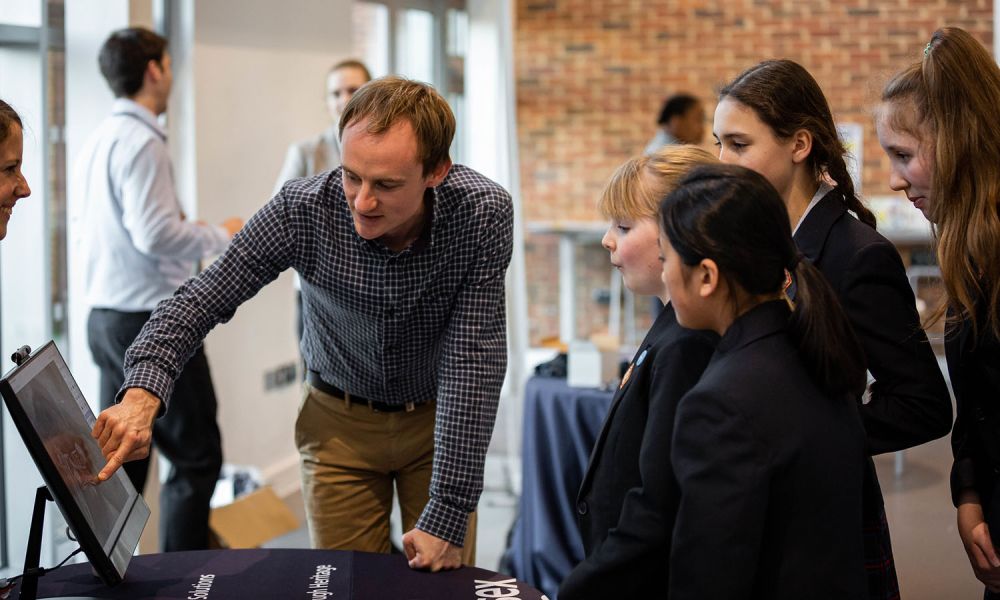 Schoolchildren stand around a screen while a demonstrator points out interesting features.