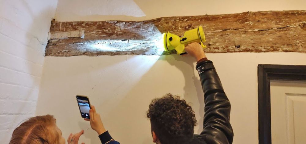 A buildings archaeologist holds a torch to a wooden beam to reveal incised marks.