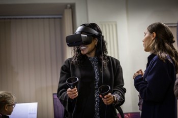 A woman uses a VR headset and handheld wands during a demonstration session.