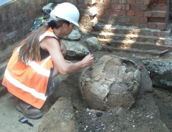 An archaeologist excavates a large spherical ceramic.
