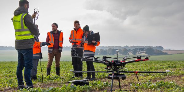 Archaeologists stand next to a drone and plan a flight in a green landscape.