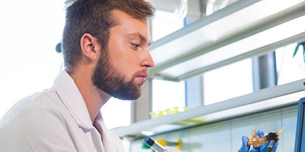 A laboratory technician in a white lab coat examines a small piece of bone.