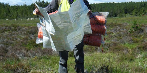 An archaeologist stands in a moorland landscape and examines a map.