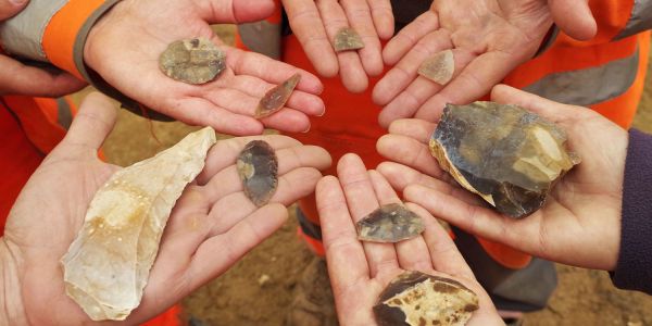 Hands holding flint tools are held together in a circle.