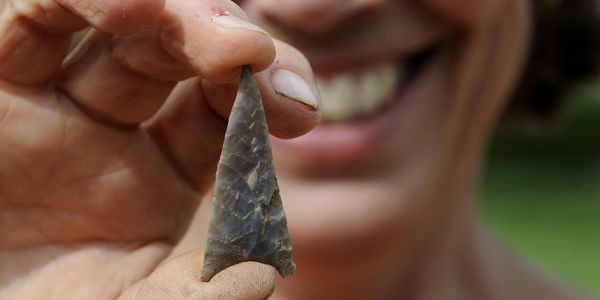 A close up of an archaeologist's hand holding a flint arrowhead.