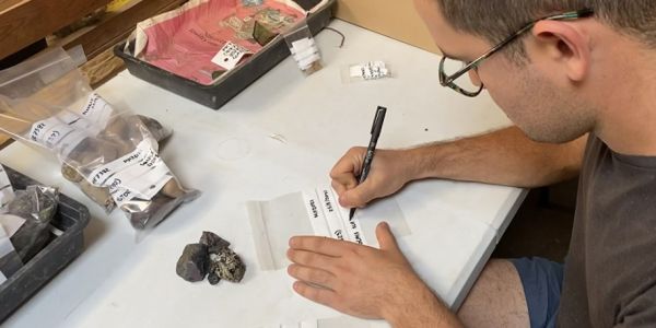 An archaeologist writes on clear plastic finds bags at a desk.