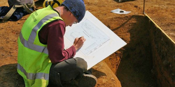 An archaeologist records an excavated trench using a pencil and paper.