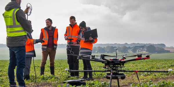 Archaeologists stand next to a drone and plan a flight in a green landscape.