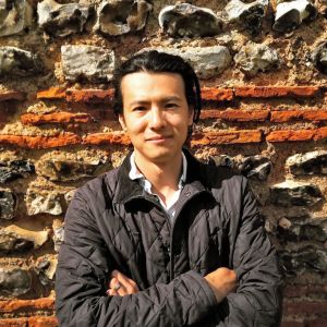 Han Li stands in front of an ancient wall of stone and brick.