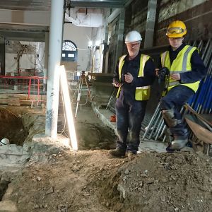 Stuart R Taylor stands beside an excavated trench inside a building.