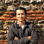 Han Li stands in front of an ancient wall of stone and brick.