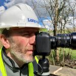 Karl Taylor looks through the viewfinder of a digital camera.