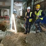 Stuart R Taylor stands beside an excavated trench inside a building.