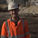 Photograph of Alex on site, wearing orange high vis and a white hard hat